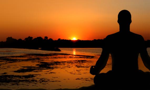 A person meditating at sunset by the water